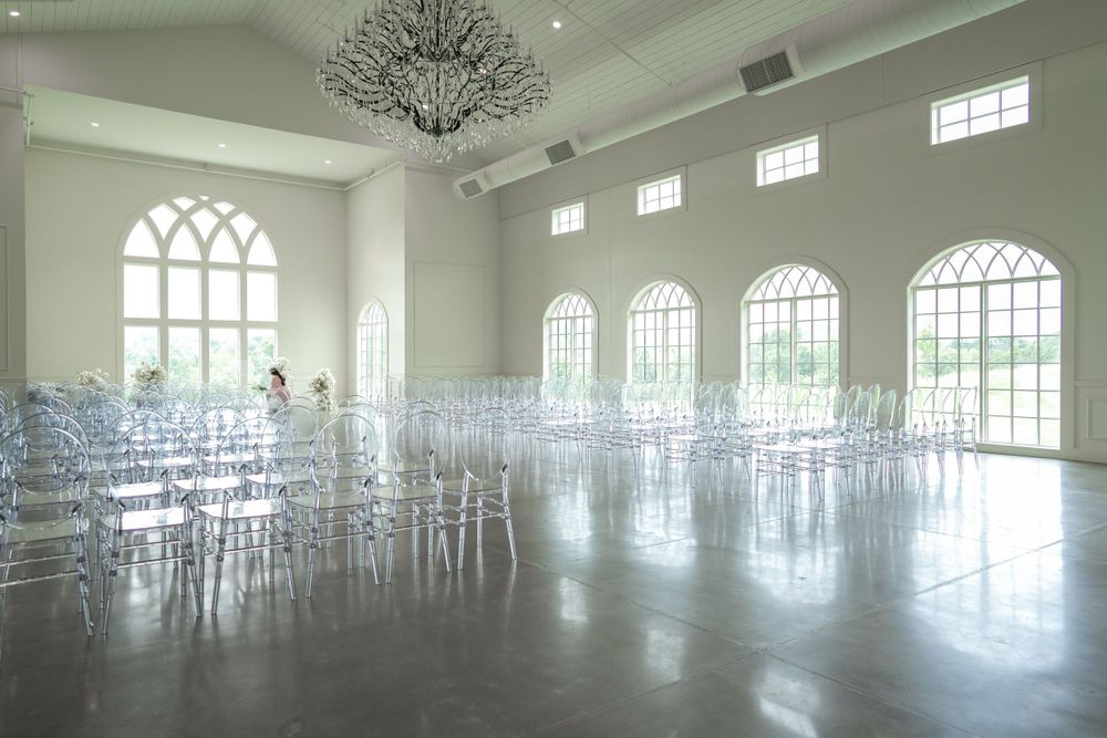 An elegant white wedding venue with crystal chandelier and clear chairs set up for a ceremony.