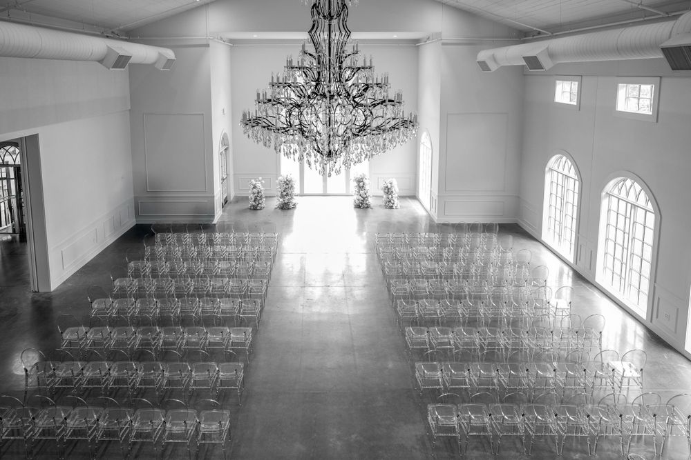 Black and white photo of an elegant wedding chapel with rows of chairs and grand chandelier.