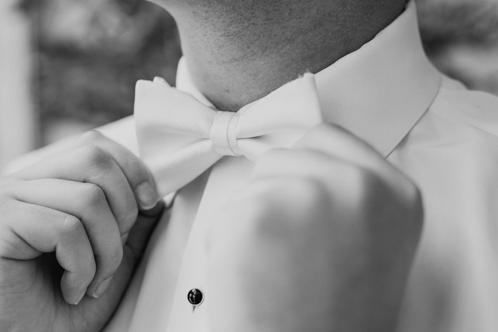 Close-up black and white shot of hands adjusting a white bow tie.