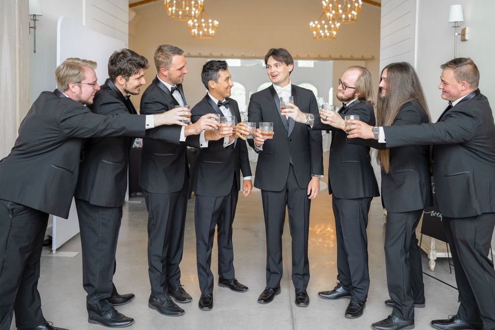 Groomsmen in black suits gather for a celebratory toast before the wedding ceremony.