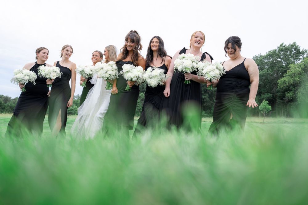 Wedding party poses with white bouquets in grass field on cloudy day.