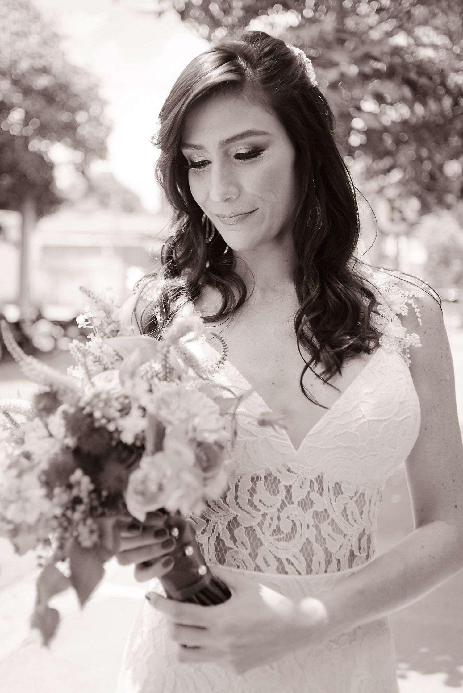 Black and white bridal portrait shows bride in lace wedding dress holding floral bouquet while looking down thoughtfully.