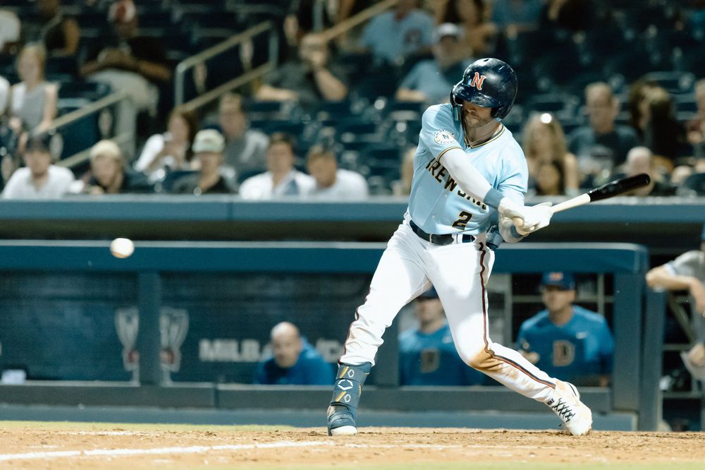 Professional baseball player in white uniform with blue pinstripes swings at pitch during MLB game.