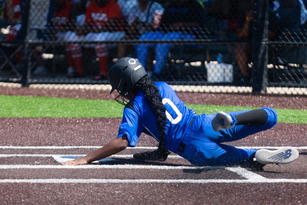 A baseball player in a blue uniform slides into home plate during a game on a dirt field.