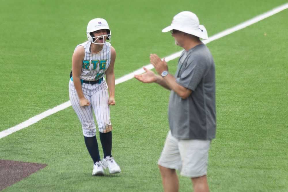 A baseball player in a striped uniform stands on the field while receiving instruction from a coach in a gray shirt.