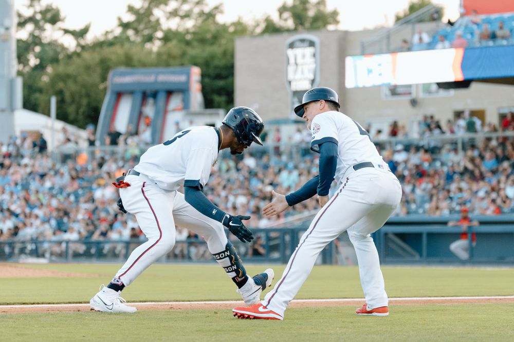 Baseball players compete at first base during a professional game with spectators in the stadium background.