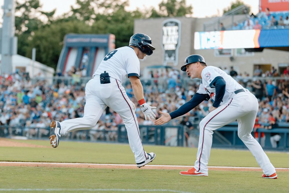 Baseball players in action during a game as runner sprints toward first base while fielder prepares to make a play.