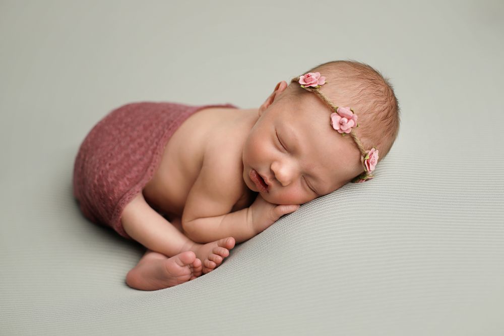 Sleeping newborn in pink wrap posed on grey backdrop during professional photo session.