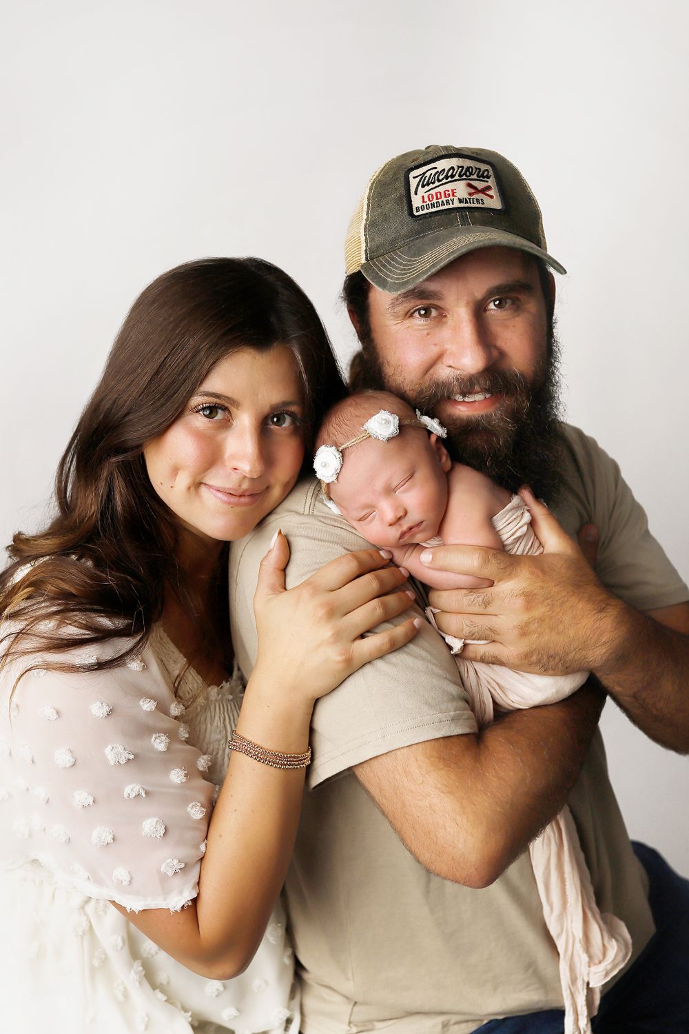 A family portrait against a white background showing a couple and their sleeping newborn baby.