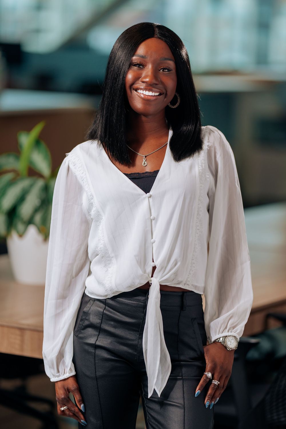 Professional in white blouse and dark pants standing in modern office setting.