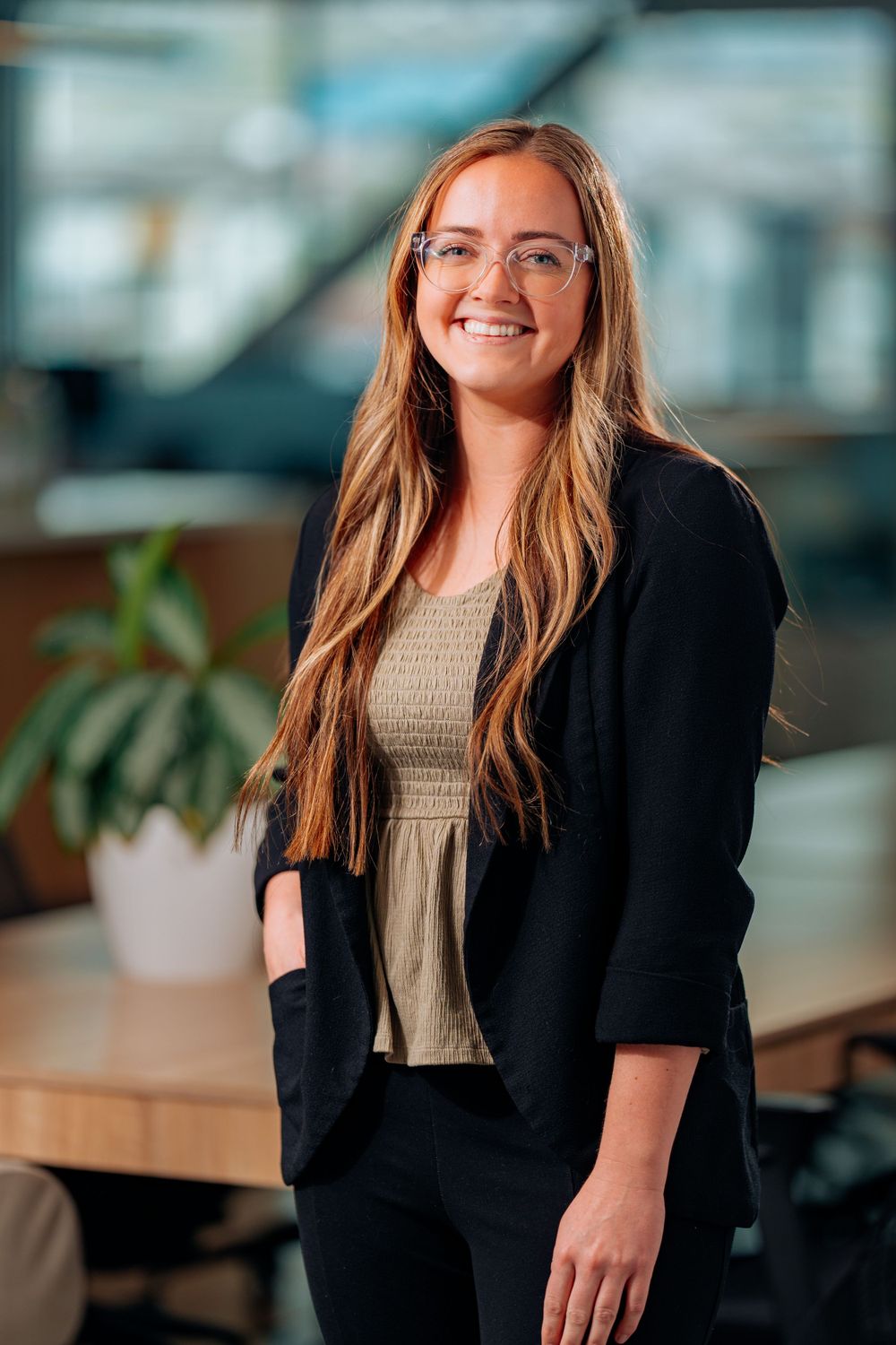 Professional in business attire standing in modern office with plants.