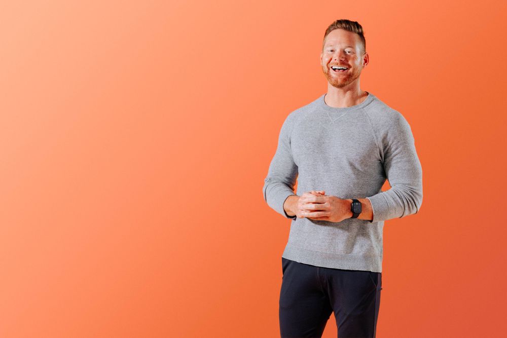 Professional in grey sweater standing against orange background.