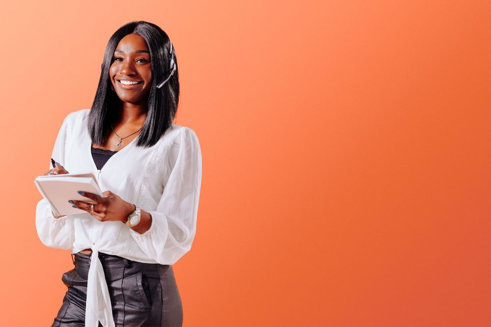 Professional wearing headphones and white blouse holding tablet against orange background.