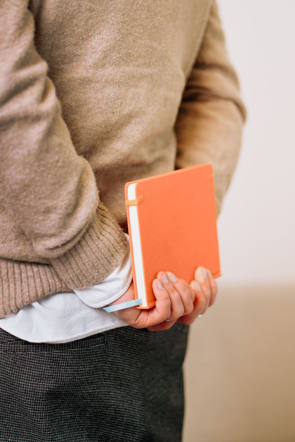 Person holding an orange notebook while wearing a beige sweater.