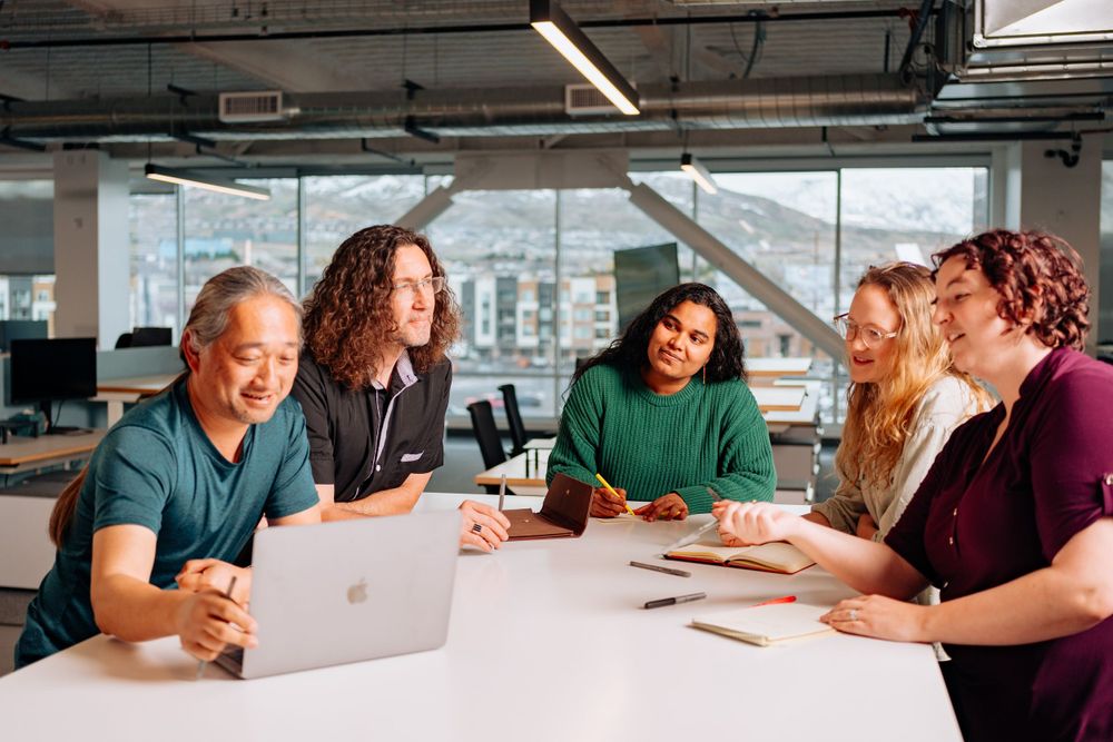 Group of diverse professionals collaborating around a laptop in modern office setting.