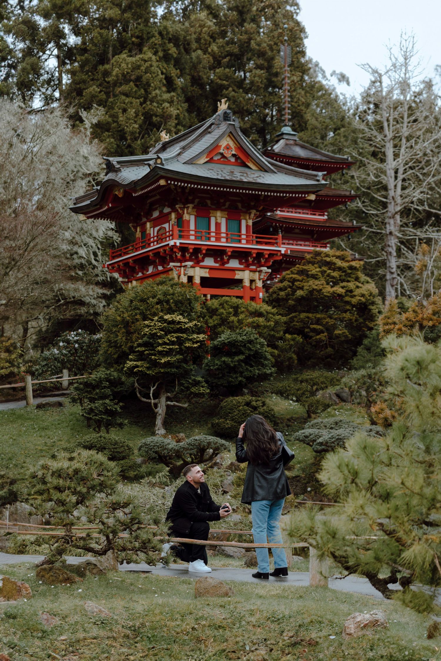 Traditional Japanese temple garden with couple admiring ornate red pagoda architecture.