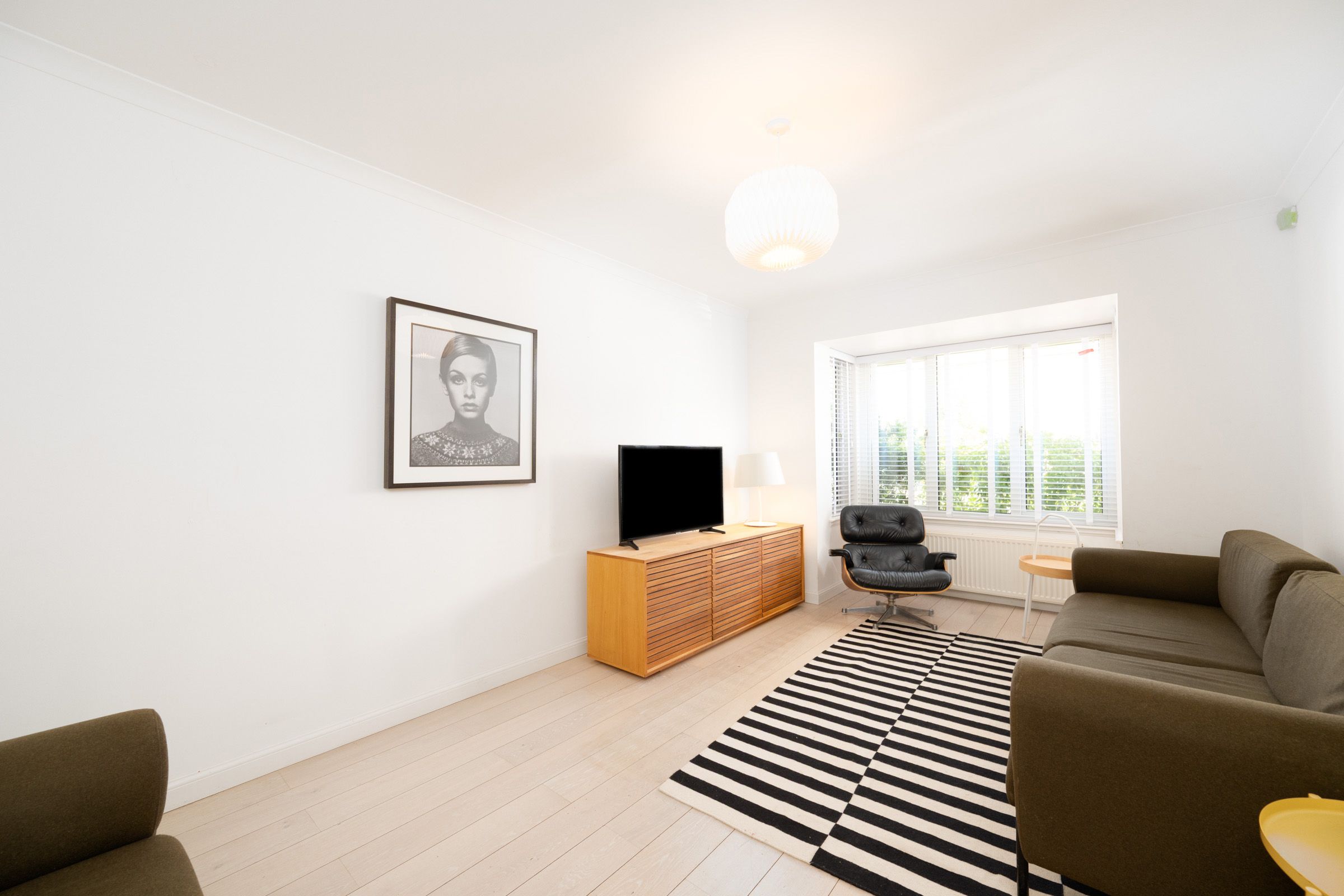 Modern living room with black and white striped rug, grey sofa, wooden media unit and large window.