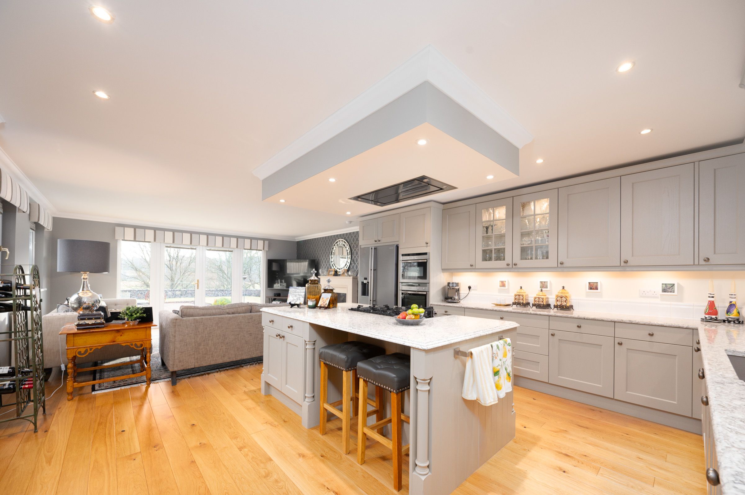 Modern open concept kitchen with grey cabinets, center island, hardwood floors and recessed lighting in bright interior.