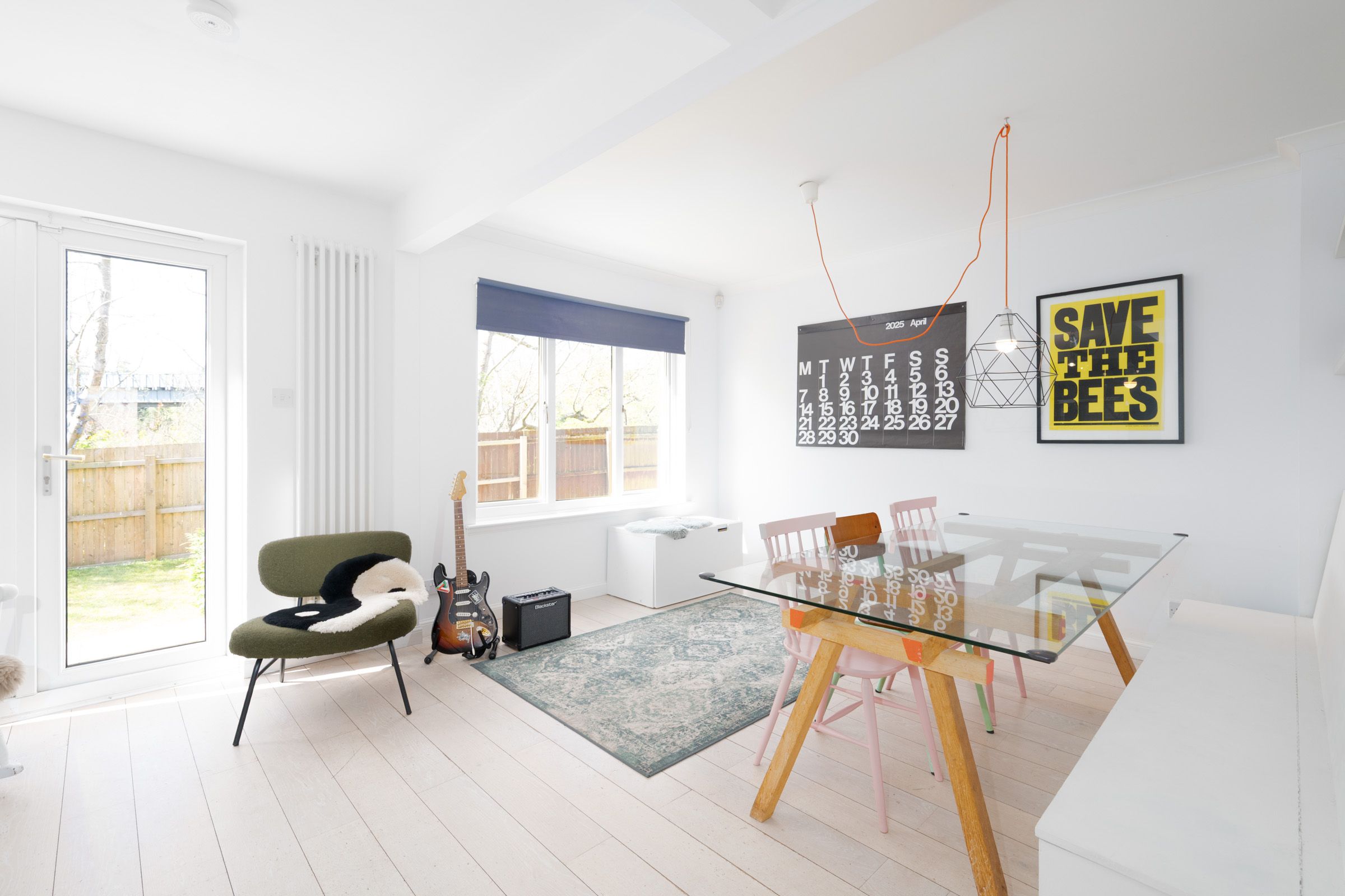 Modern minimalist living room with glass dining table, green accent chair, wooden floors, and clean white walls.