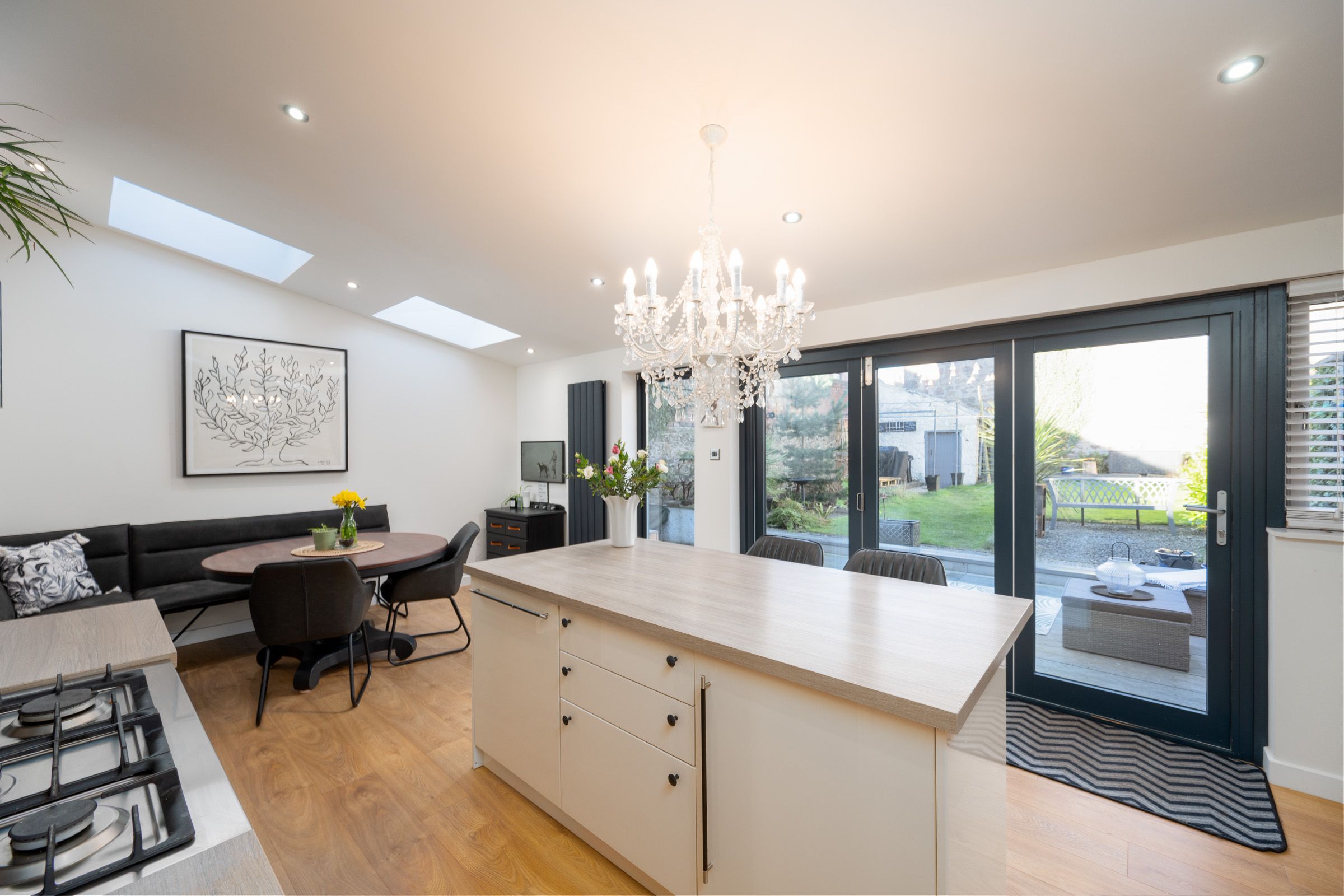 Modern open concept kitchen with white countertops, glass doors, skylights and crystal chandelier in luxury home interior.
