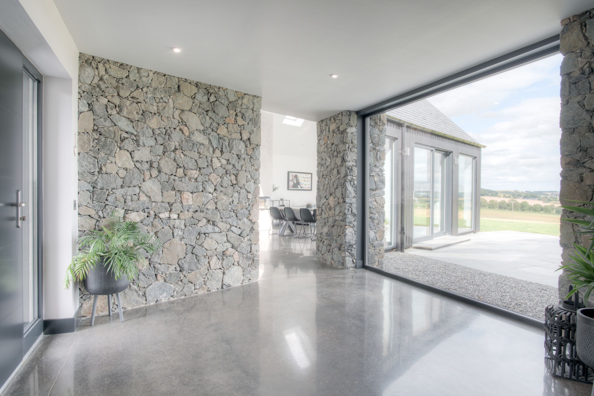 Modern interior room with stone accent wall, polished concrete floor and large glass windows overlooking a landscape view.