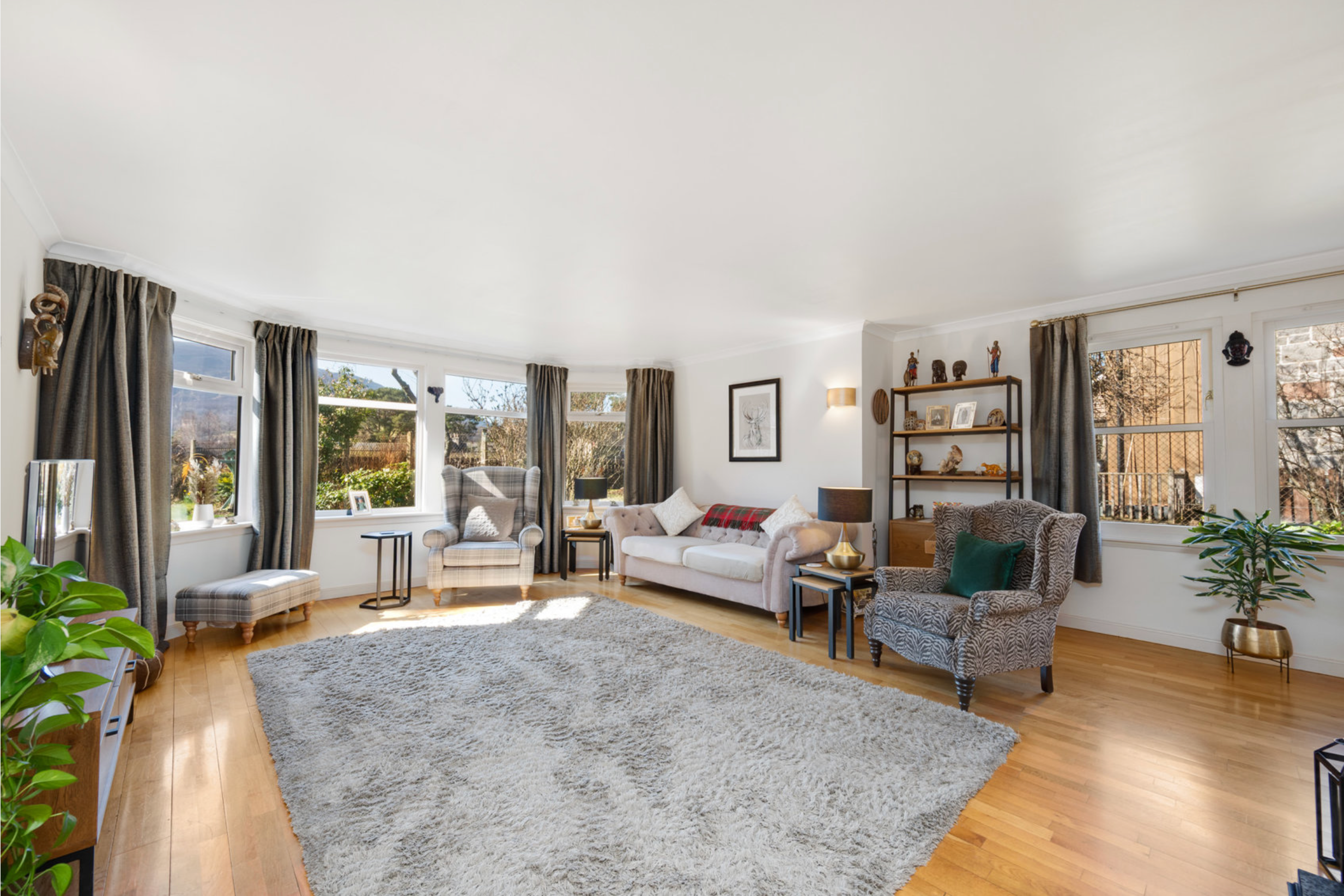 Modern living room with hardwood floors, gray area rug, plush furniture, and large windows bringing in natural light.