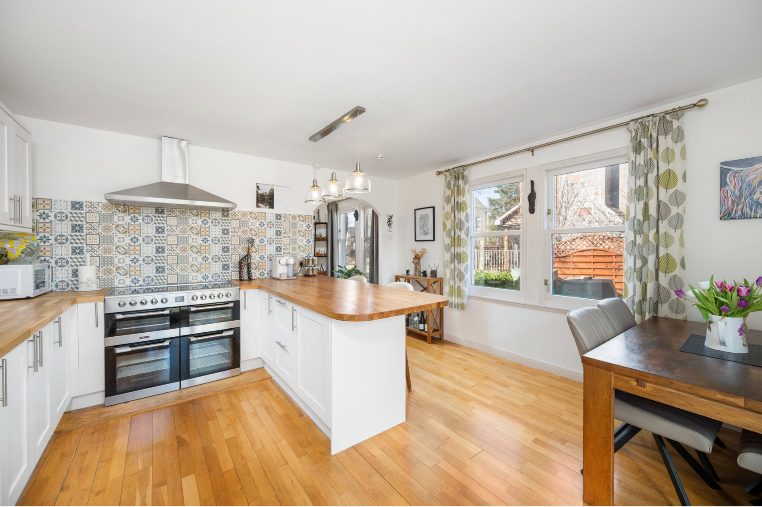 Modern open concept kitchen with white cabinets, wood floors, geometric tile backsplash and dining nook by window.