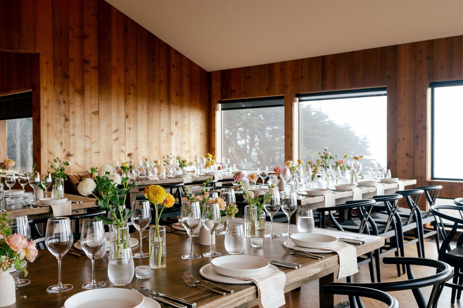 Elegant wedding reception table setting with wooden walls and large windows at the Sea Ranch Lodge Dining Room.