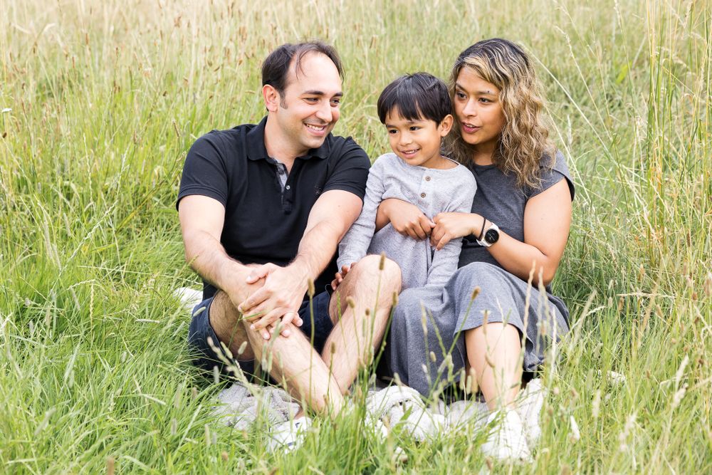 family of three sitting on the grass in the park