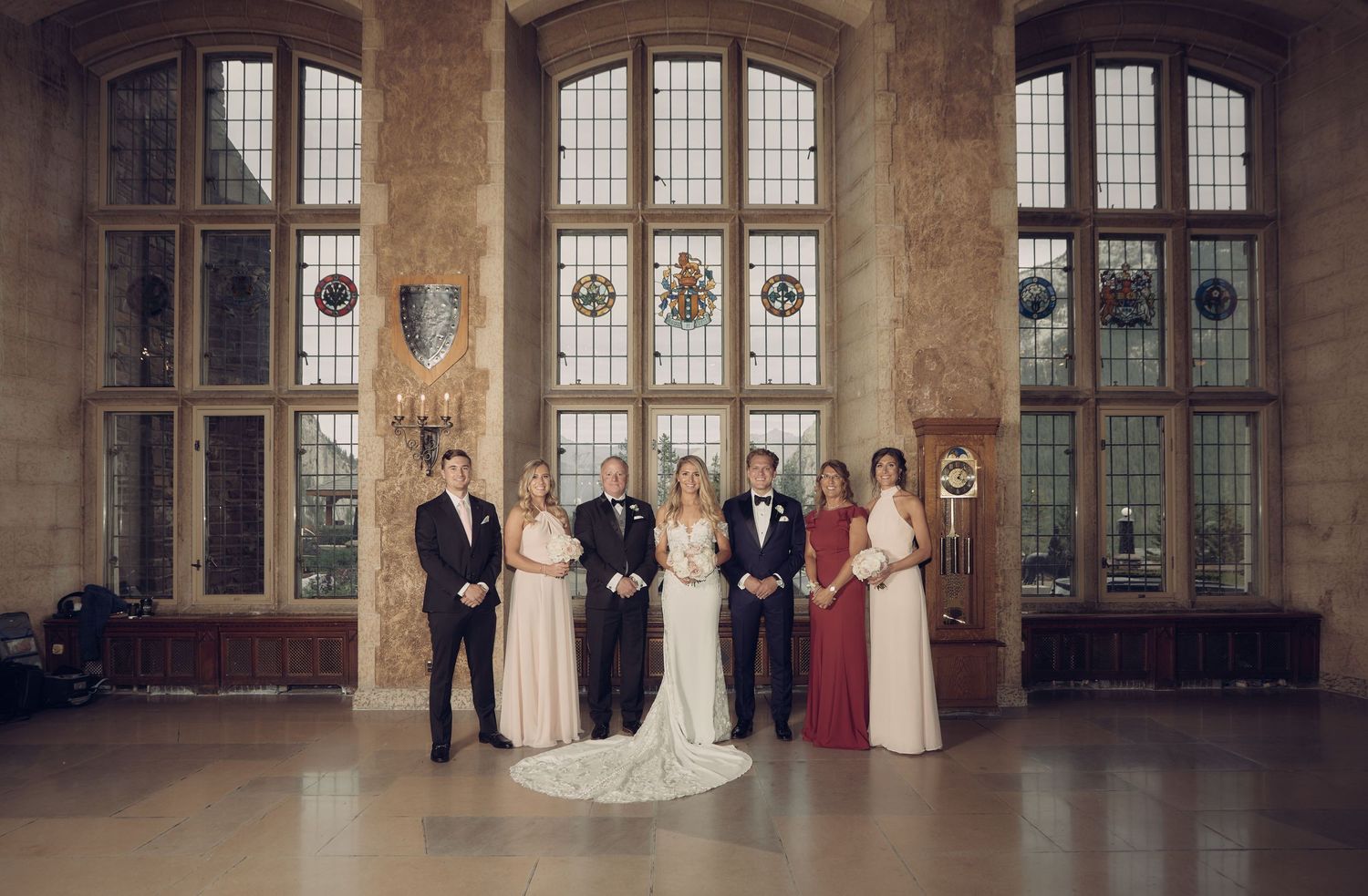 Elegant wedding party poses in front of grand arched windows in a Banff Springs Hotel with ornate architectural details in Mt. Stephen Hall