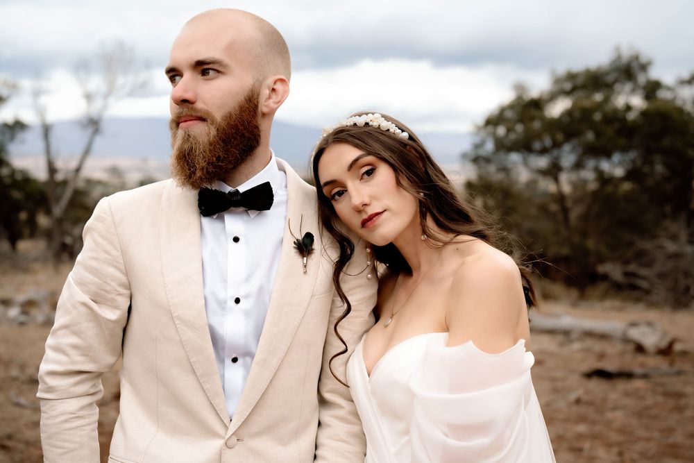 A couple poses together in formal wedding attire against a desert landscape backdrop.