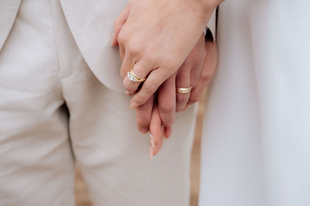 Close-up of a hand wearing an elegant engagement ring against a light beige background.