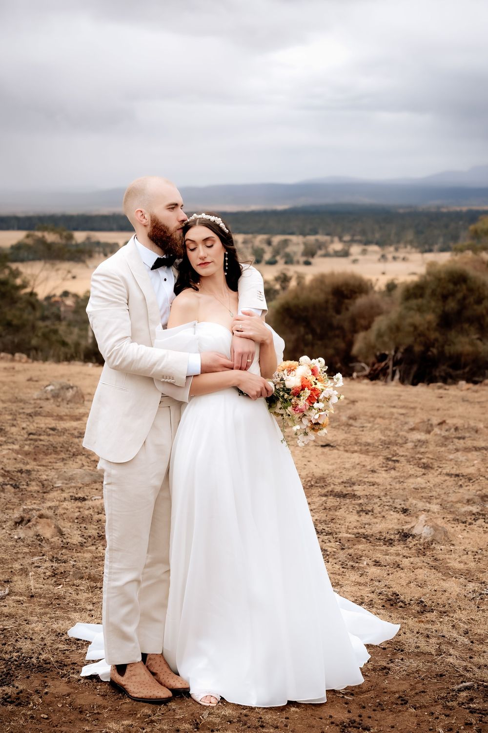 A couple shares an intimate moment in their wedding attire against a scenic mountain landscape backdrop.