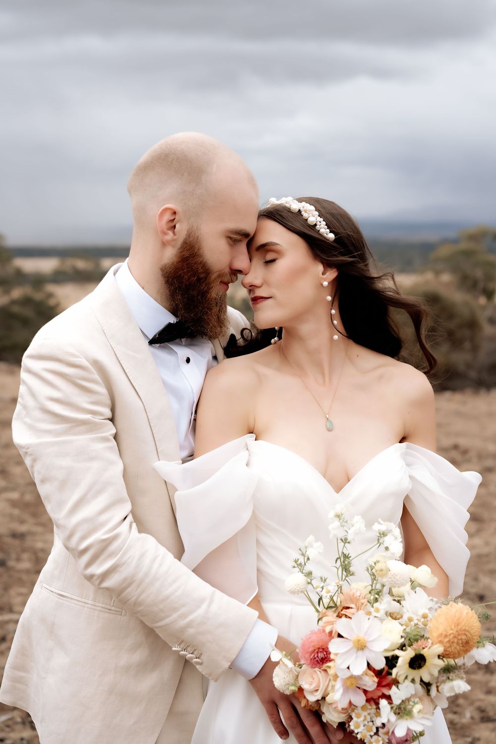 A romantic wedding couple embraces in an intimate moment against a desert landscape with the bride holding a white bouquet.