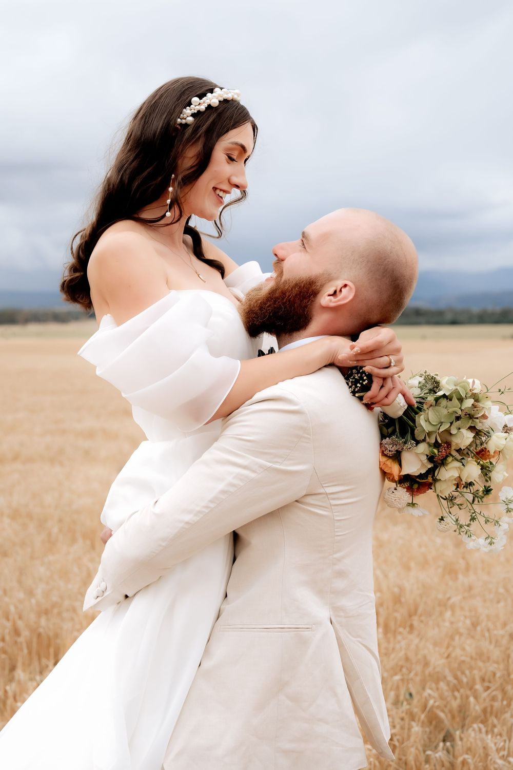A joyful wedding moment captured as a couple in white share an intimate embrace in a golden field.