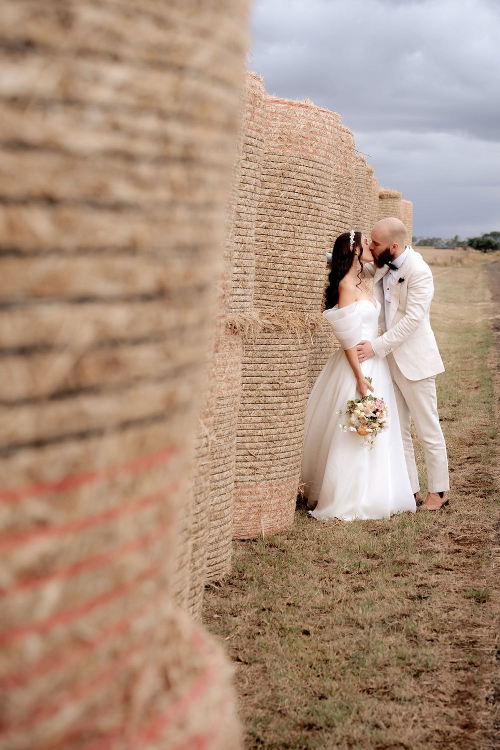 A newlywed couple embraces beside a rustic stone wall during their outdoor wedding photoshoot.