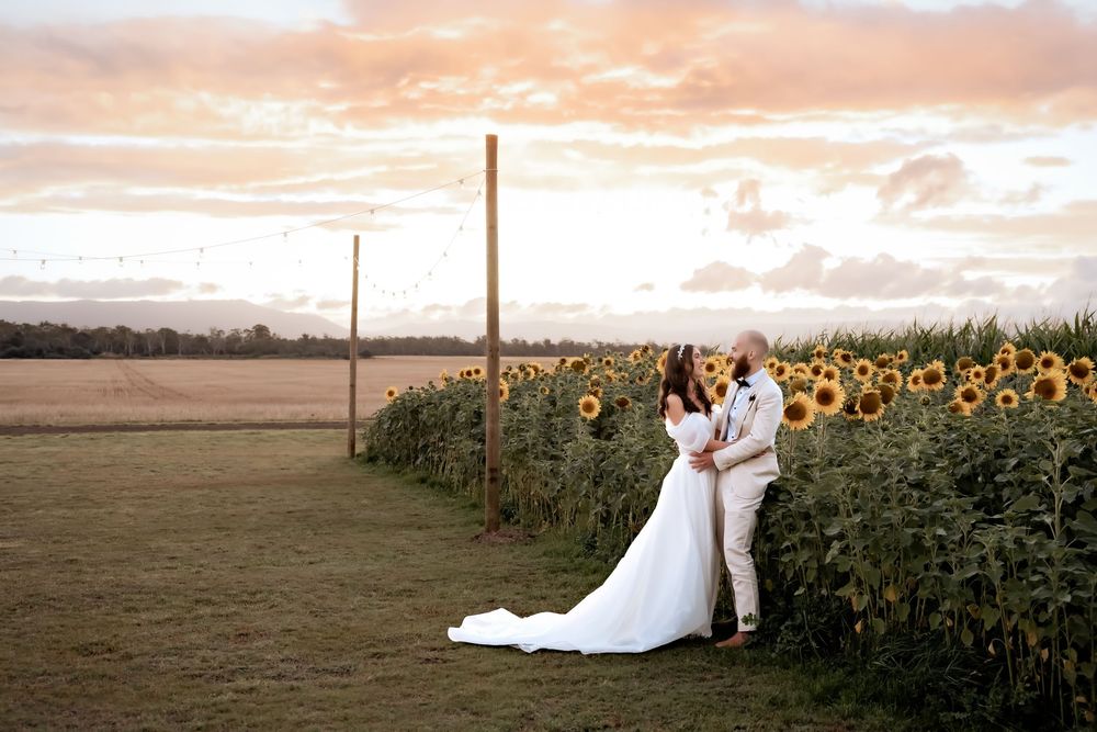 A romantic wedding portrait at sunset with the couple standing beside a field of sunflowers.