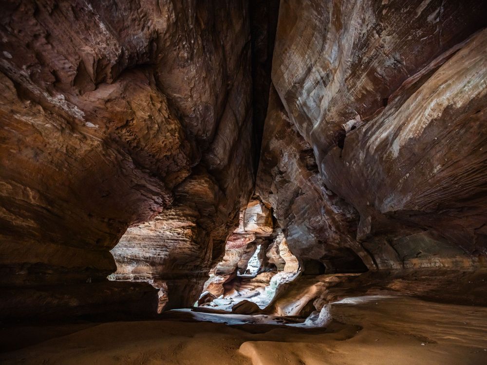 Dramatic natural rock formations and layered sandstone walls inside a dark underground cave with water reflections.