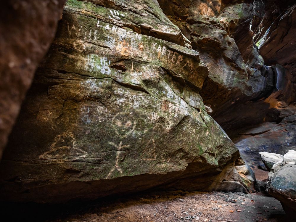 Ancient Native American petroglyphs carved on sandstone rock wall inside natural cave formation.