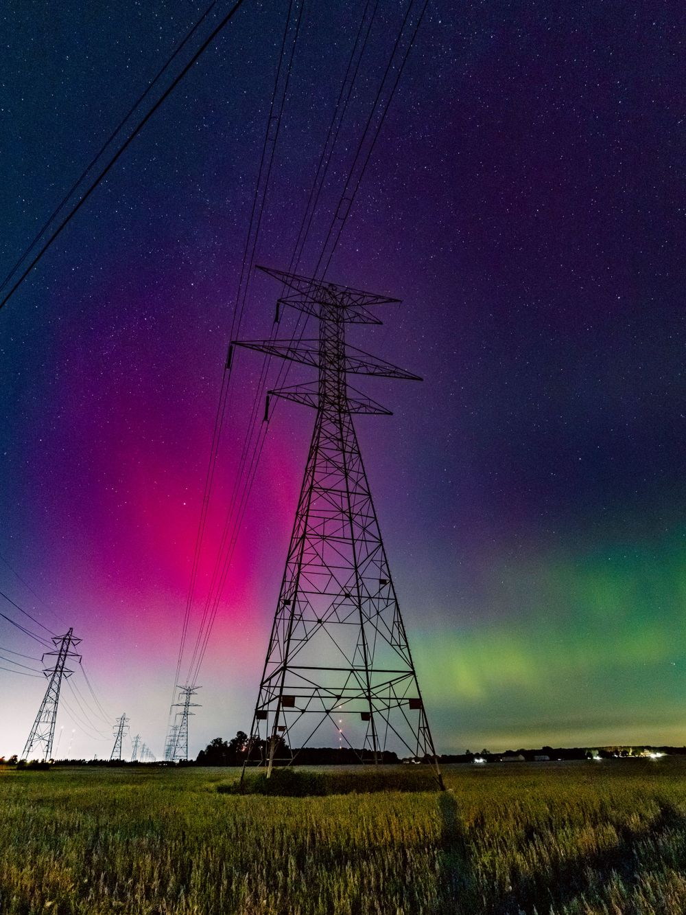 Electric transmission towers silhouetted against vibrant purple and green aurora borealis in the night sky.