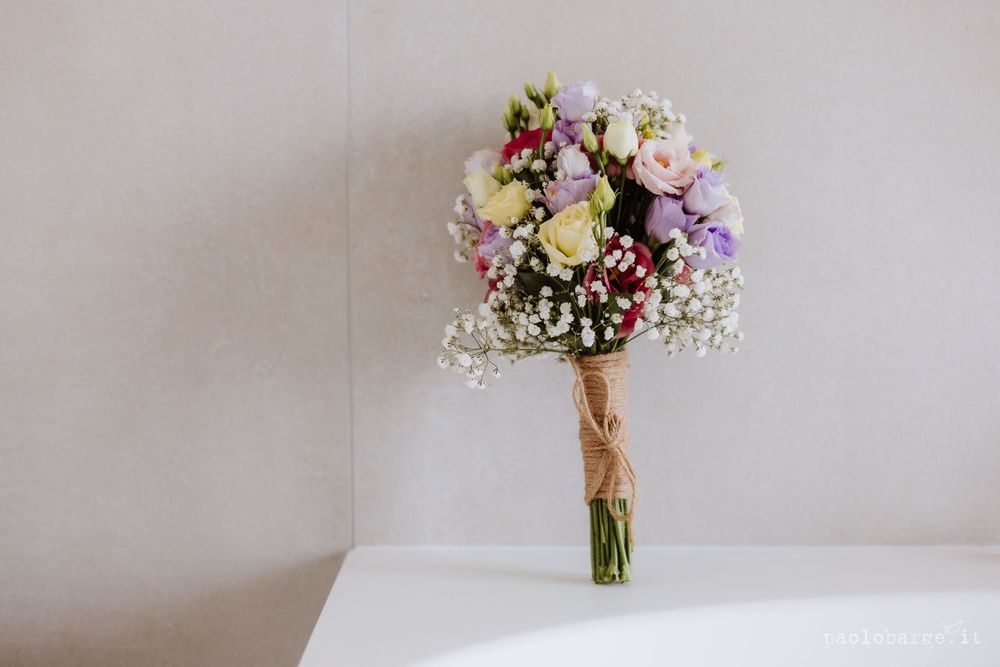 Elegant wedding bouquet with purple, white and pink flowers tied with twine on white surface.