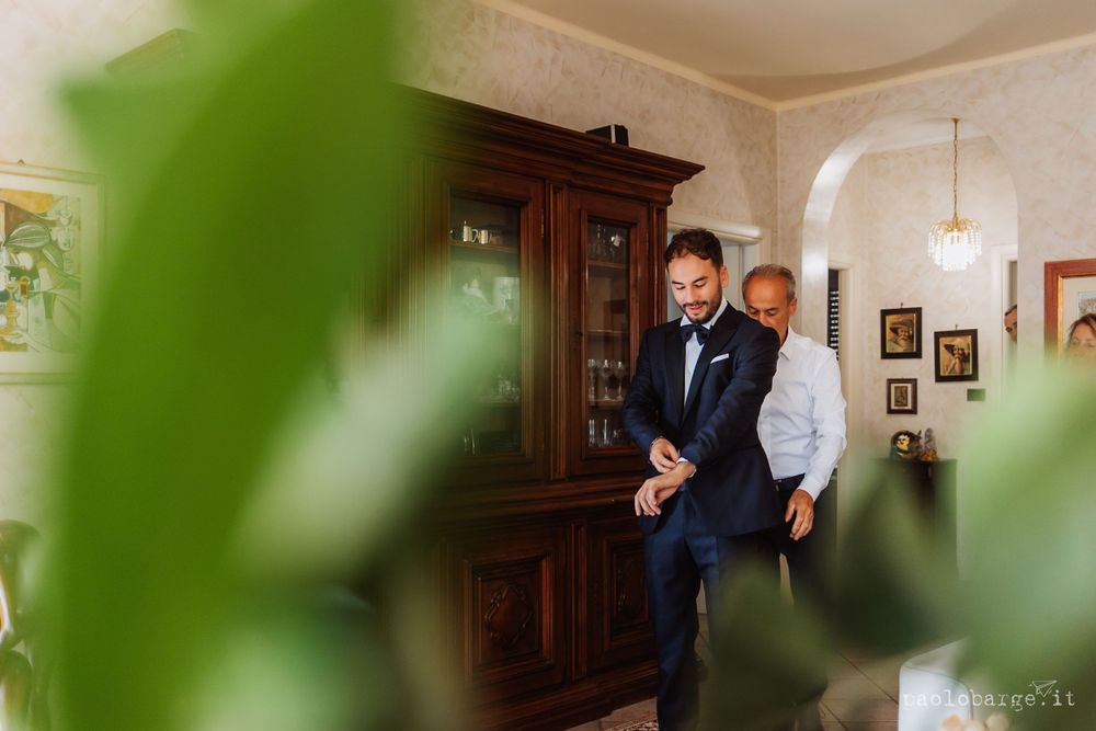 Two people in formal attire standing by a wooden cabinet in a traditional room setting.
