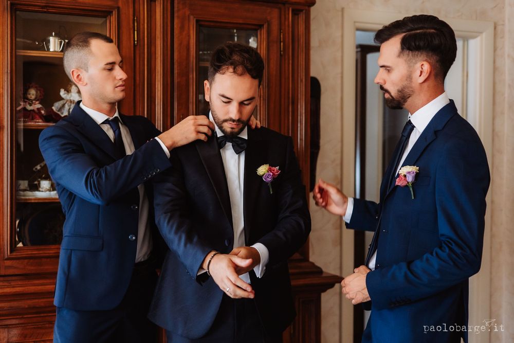 Three men in blue suits helping adjust formal wear before event.