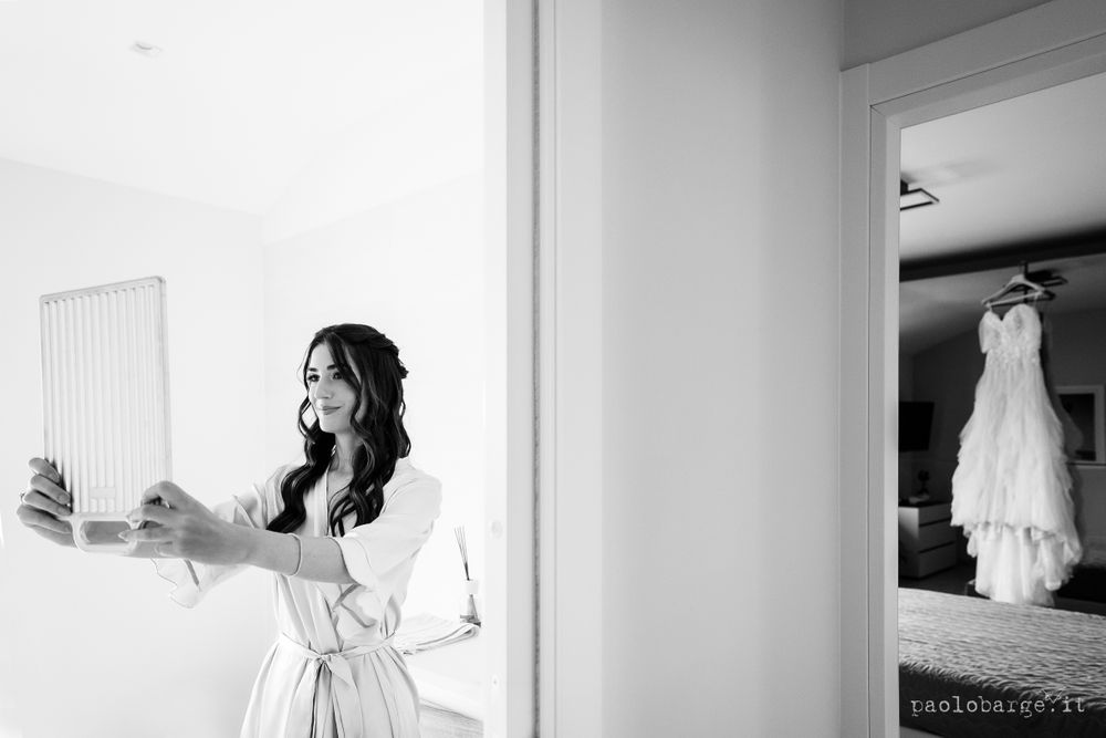 Wedding preparation scene with white dress visible hanging in background.