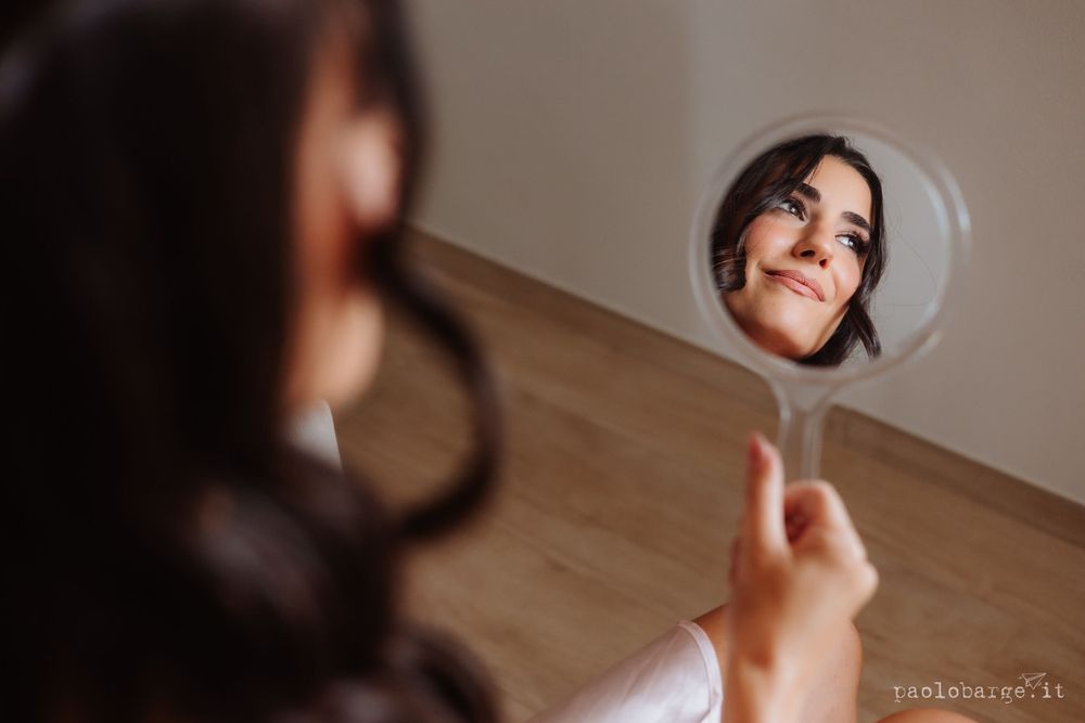Reflection of joyful expression in handheld mirror during wedding preparations.
