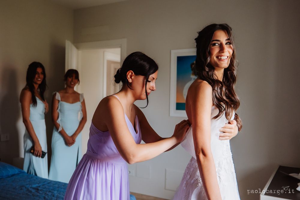 Final adjustments being made to a wedding dress as bridesmaids look on.