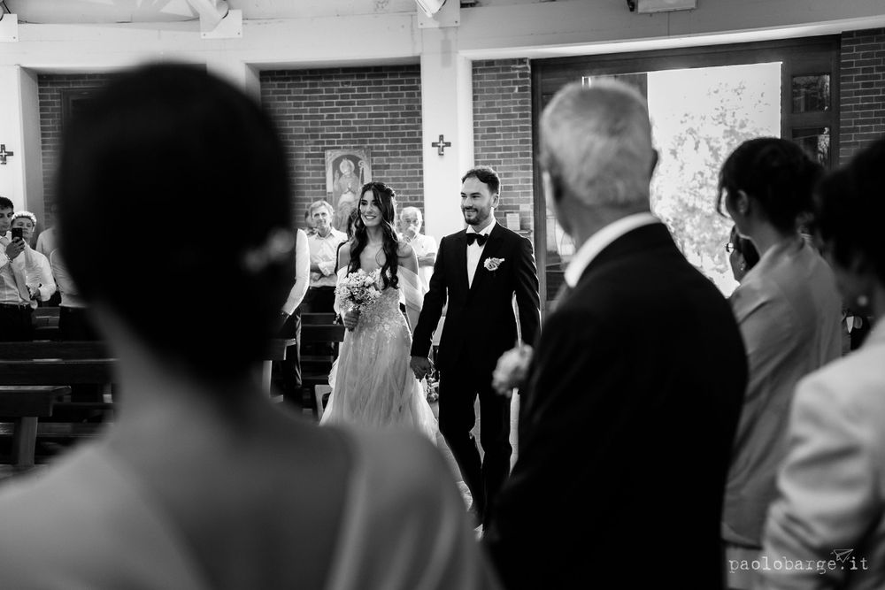 A black and white photograph captures an intimate moment during a church wedding ceremony.