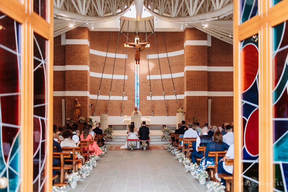 Modern church interior with stained glass windows and wooden pews decorated for a wedding ceremony.