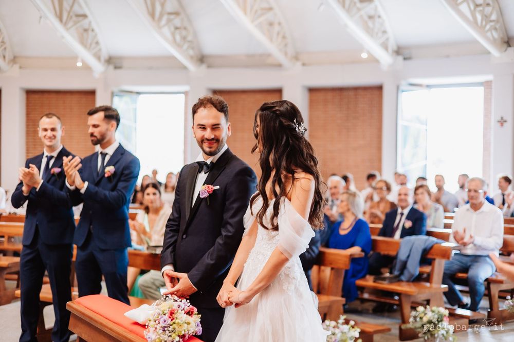 Wedding ceremony in a modern church with ornate white ceiling and guests seated in pews.