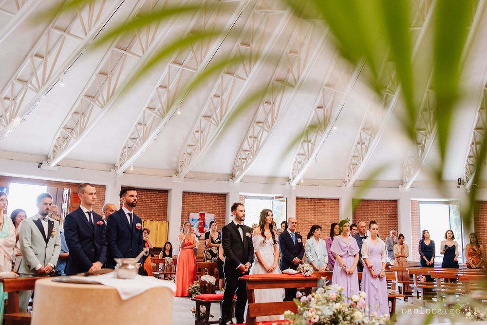 Church wedding ceremony with guests standing under decorative white vaulted ceiling.